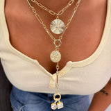 Gold chain necklace with circular pendants on a person wearing a beige top and blue jeans.